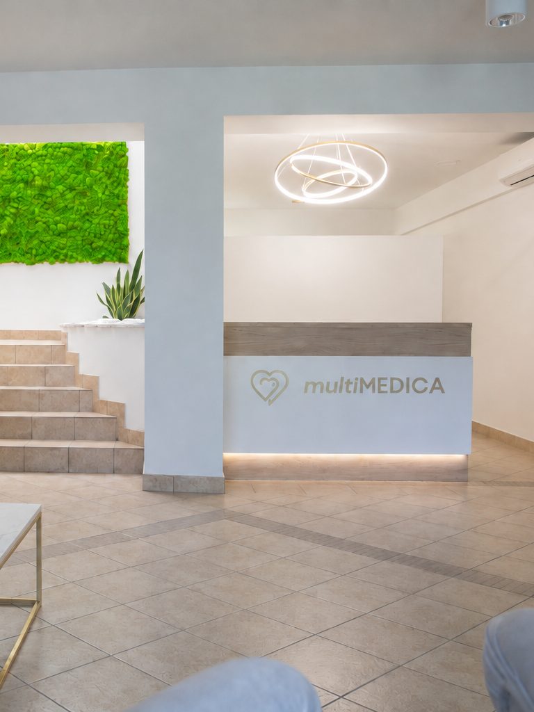 Recepcja multiMEDICA: biała lada z logo i okrągłą lampą nad nią, obok schody i ściana z zielonego mchu